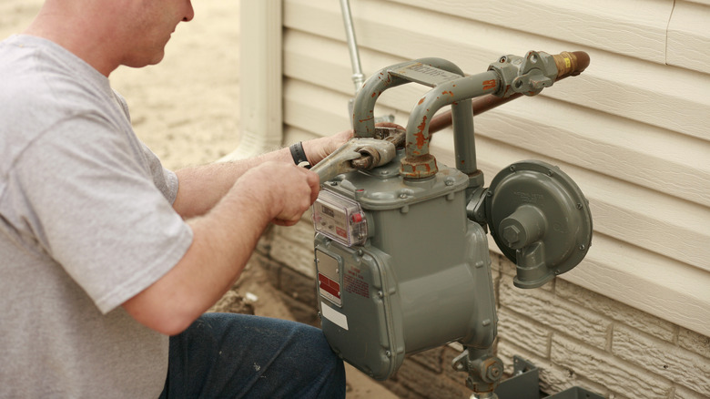 Man using a wrench on a water meter outside a house