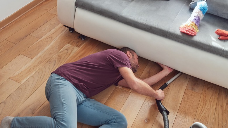 A man cleans under his couch