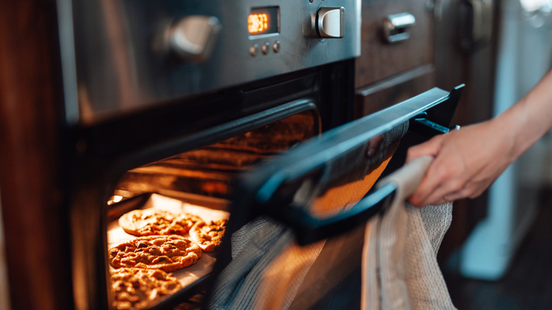 Hand opening oven door to display baking cookies