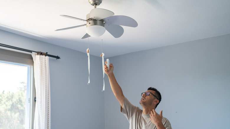 Man using remote control to turn on ceiling fan