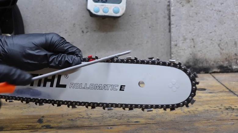 person sharpening chainsaw chain with files