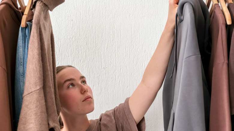 woman looking at winter clothes handing on a rail considering what to keep