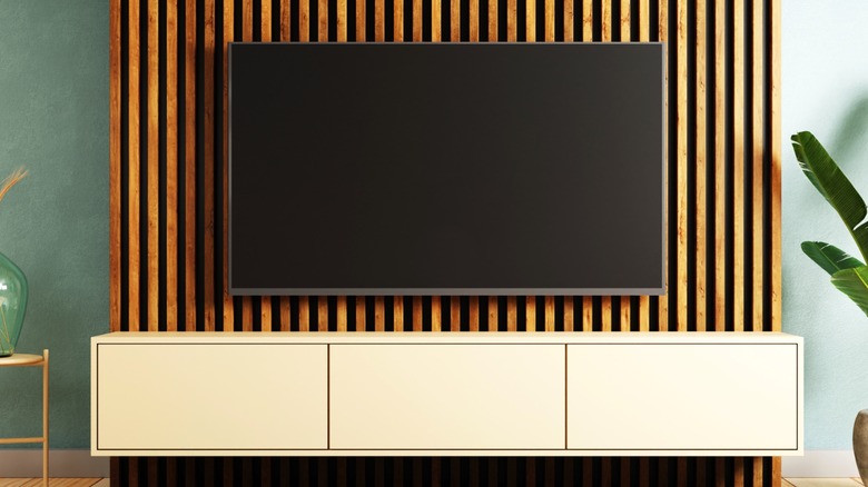 Flat screen tv mounted on wood slat wall over media console