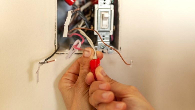 A person installing red wire nut on wiring for light switch