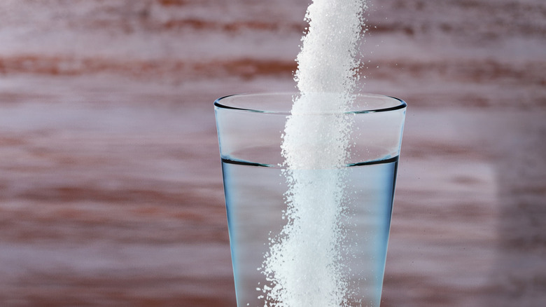 White powder being poured into a glass of water