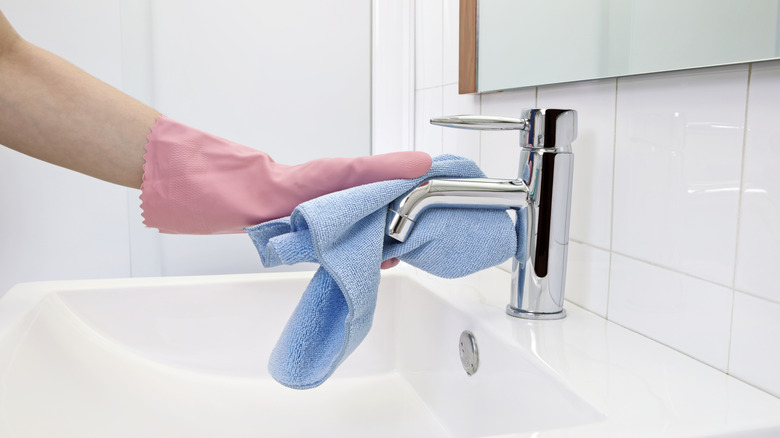 Person cleaning a faucet with a microfiber cloth