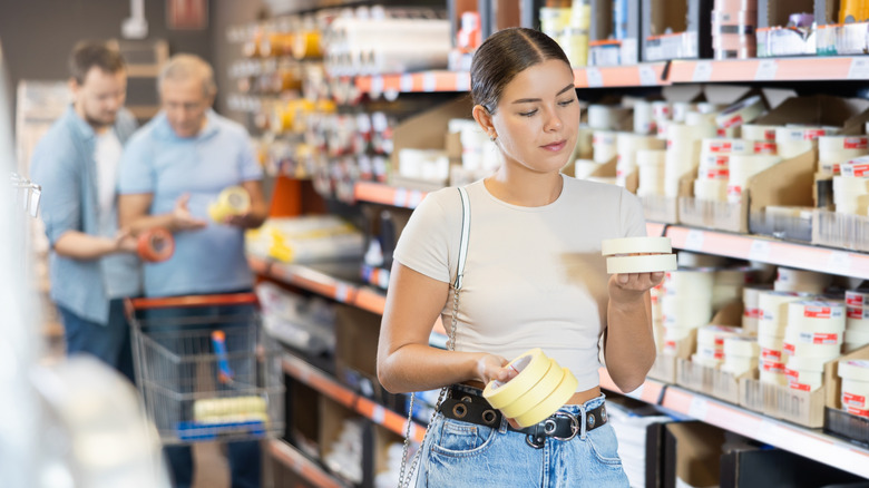 A woman holds and looks at two different kinds of tape in a store