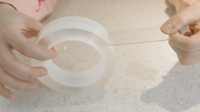 A person unrolls some clear EZLifego double-sided tape