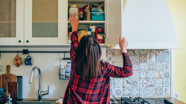 Woman reaching for jar in white kitchen cabinet