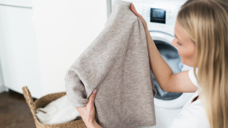 woman holding at gray clean wool sweater out of washer