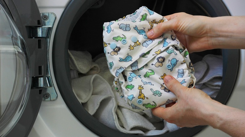 hands holding cloth diaper with animal print in front of washer