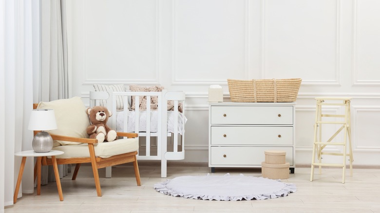 Inside of a neutral-pallette baby nursery with crib, dresser, and chair.