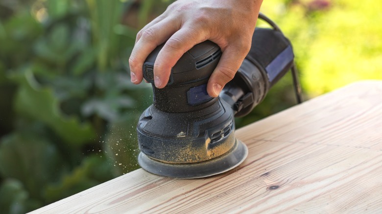 Man using palm sander on wood board.