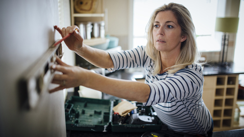 Woman using spirit level and pencil in kitchen