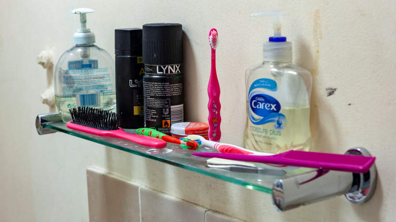 Bathroom shelf cluttered with toothbrushes, a hairbrush, and hygiene products