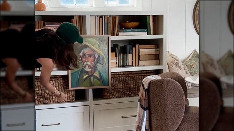 A woman displaying art on the front of a bookcase