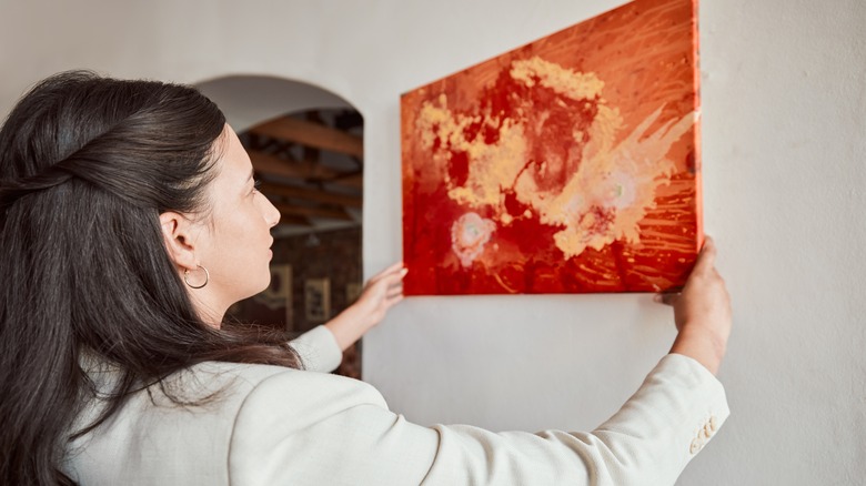 A woman hangs a picture on a wall.