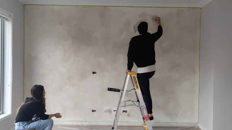 Man on a ladder applying limewash to wall