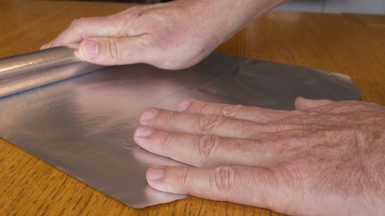 man unrolling aluminum foil