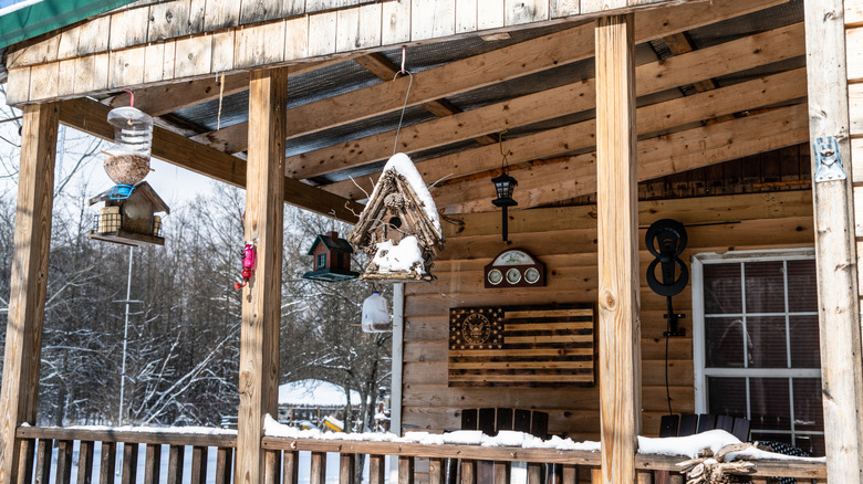 Various styles of bird feeders attached to the porch of a wooden home.