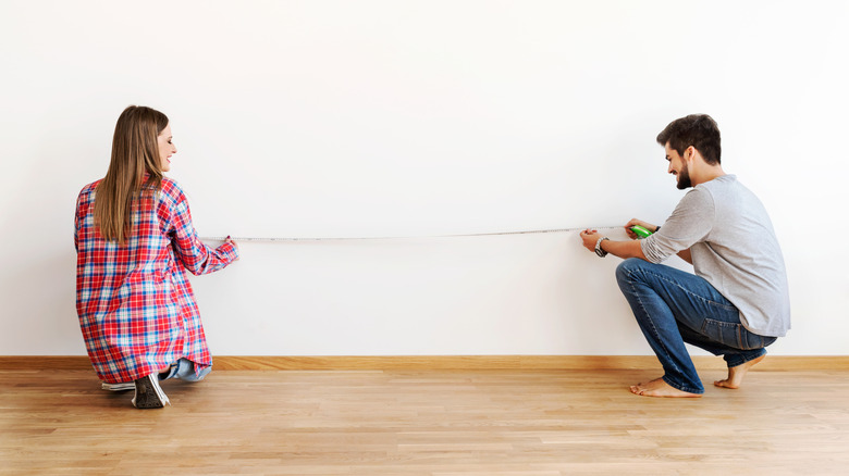 A couple measuring an empty wall in their home.