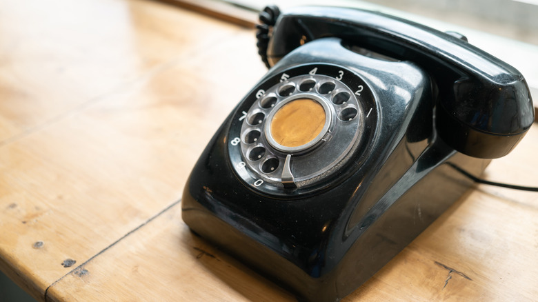 A vintage black rotary phone sitting on a wooden surface