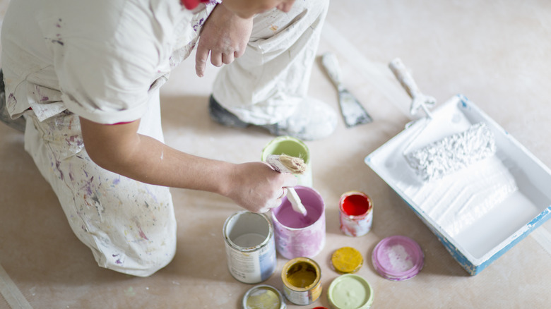 A man stirring paint surrounded by multiple paint cans