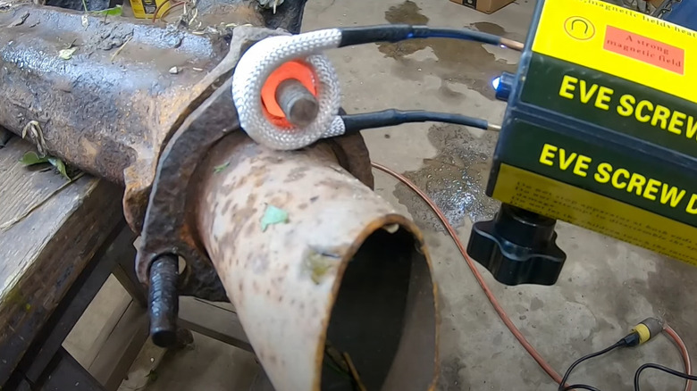 Person using an induction heater to heat up a rusty bolt.