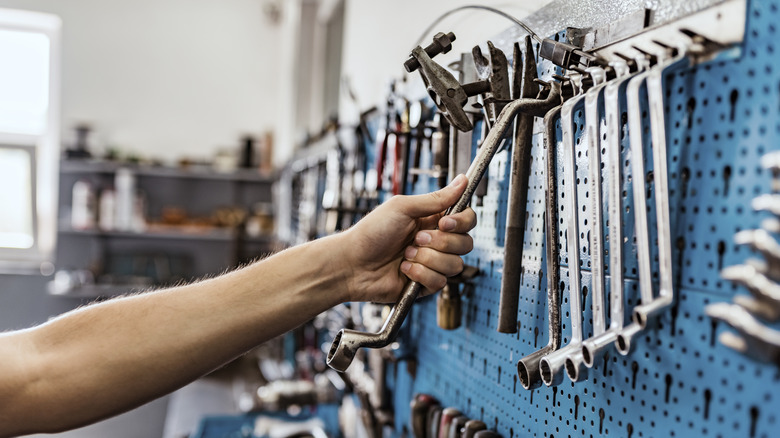 A mechanic reaching for tools arranged on the wall.