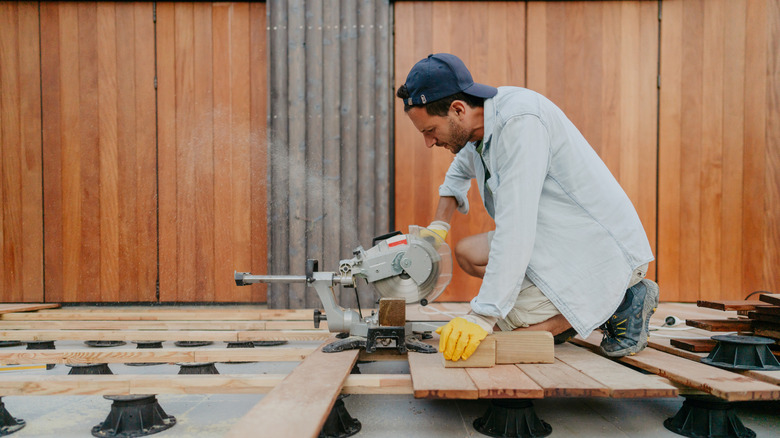 man cutting planks of wood outside with a power saw machine