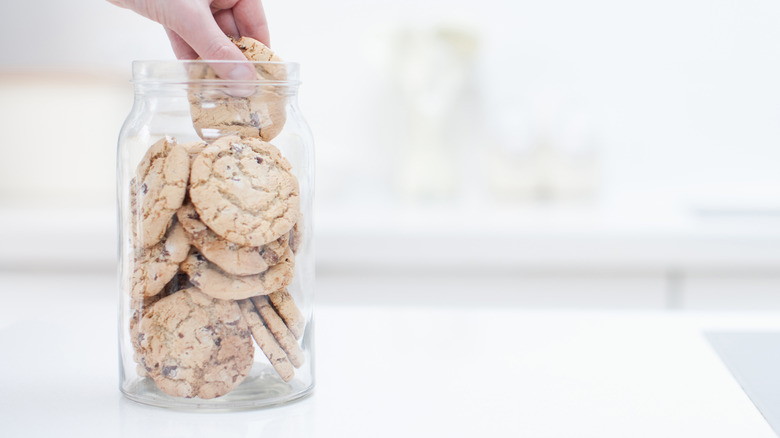 A hand reaching for a cookie inside a jar full of cookies