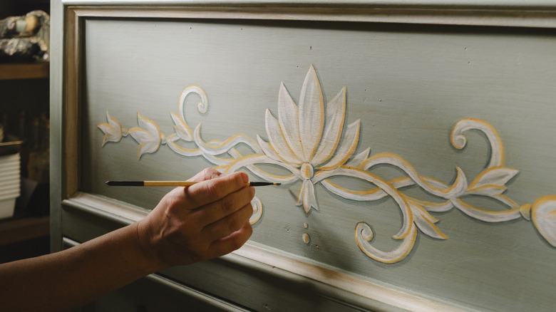 Person painting design on wooden dresser drawer