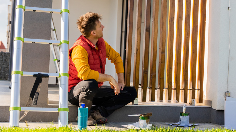 Man gazing at fence with paint materials on ground