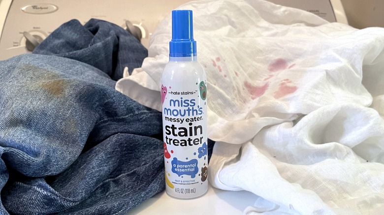 A bottle of Miss Mouth's Messy Easter Stain Treater spray sits on a washing machine surrounded by stained clothes