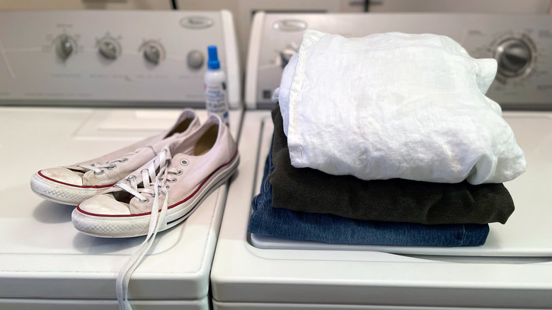 A pile of folded laundry and dingy white shoes sit on top of a washer and dryer