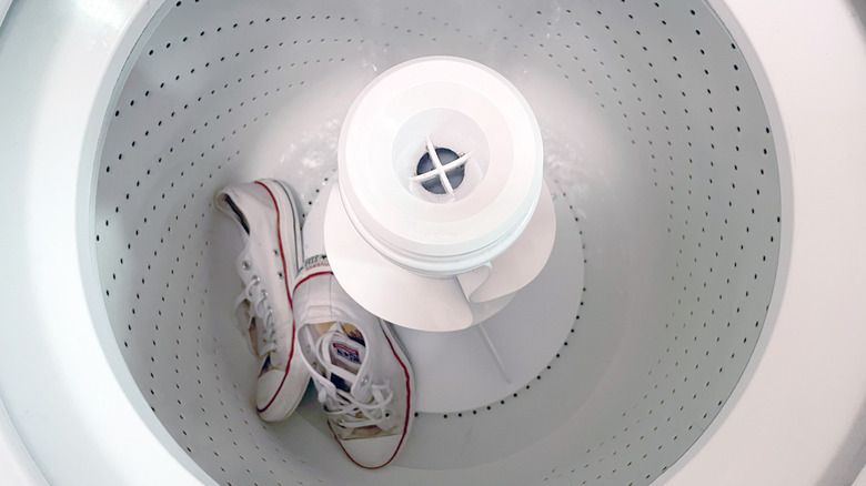 A pair of dirty white sneakers are in the bottom of a washing machine as it fills with water