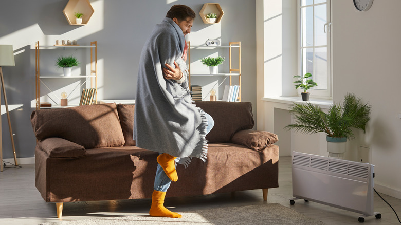 A man is cold and wrapped in a blanket inside his home