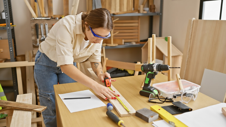 A woman measuring a piece of wood in a shop