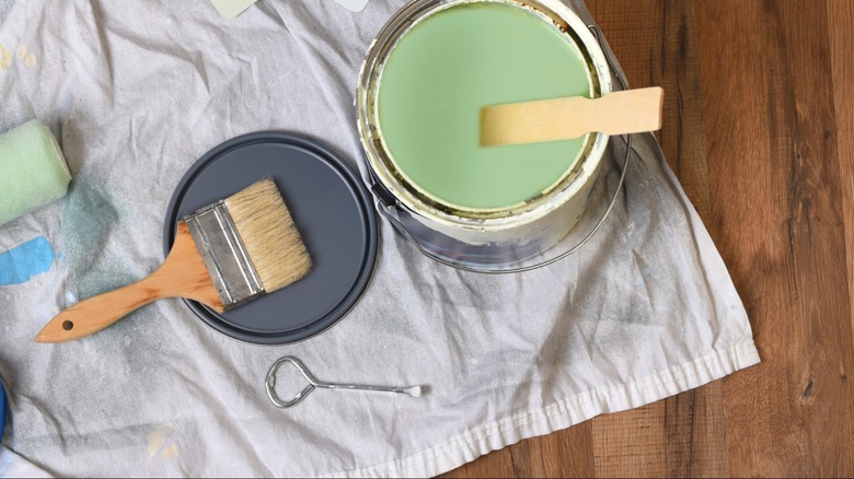 bird's eye view of green paint bucket with paint brush on drop cloth over hardwood floor