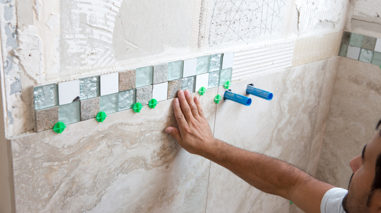 Person installing tiles and border on shower wall