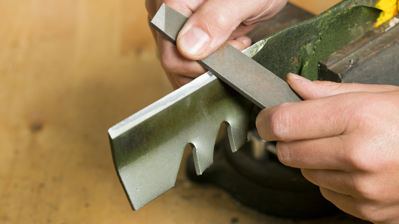 A person using a metal file to sharpen a lawn mower blade