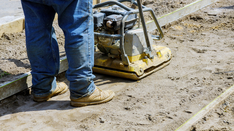 Person compacting layer of sand with machine