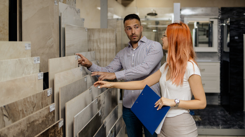 Woman holding clipboard and man look at display tiles