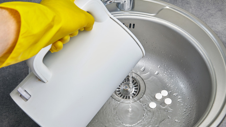 Person pours hot water in white kettle down sink