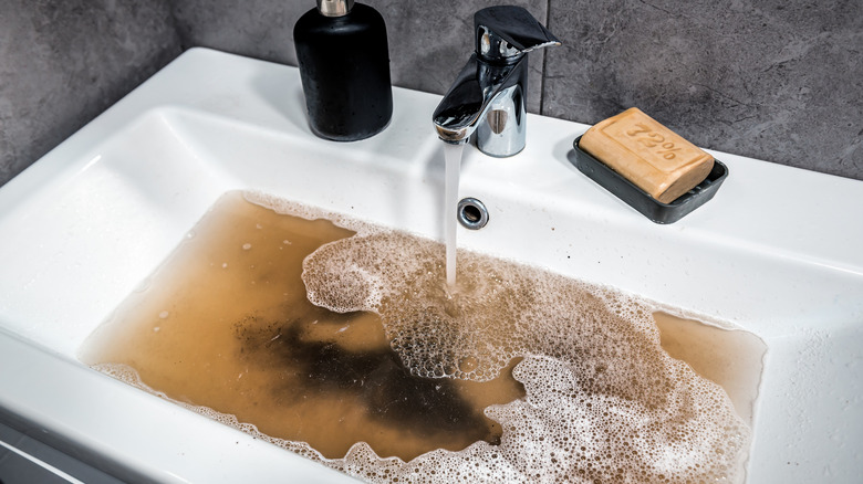 A clogged bathroom sink filled with dirty water