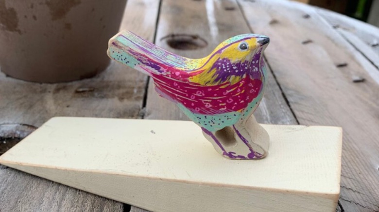 Colorful wooden bird on wedge doorstop on table