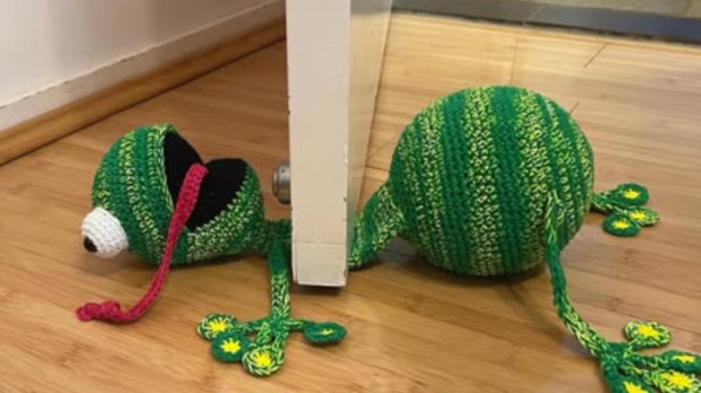 Crochet frog doorstop under door on wood floor