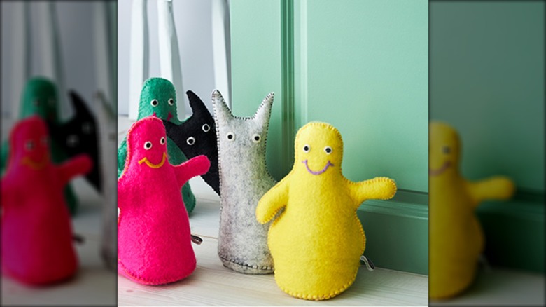 Colorful felt creature doorstops on floor in front of green door