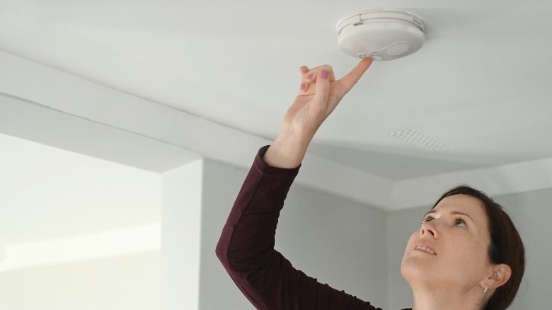 woman pressing button on smoke detector