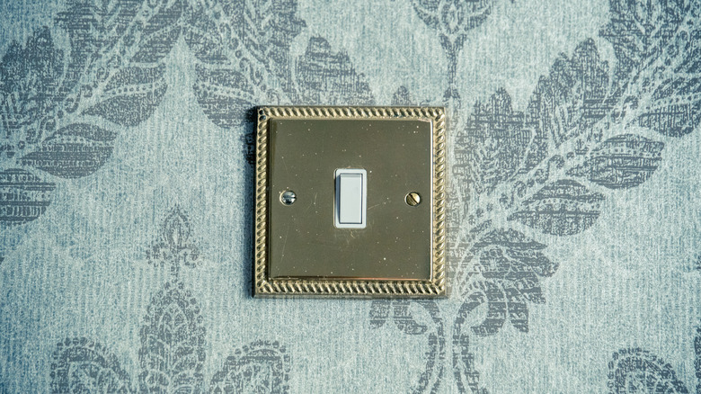 A gold light switch plate on a blue floral wallpapered wall